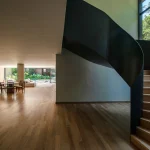 Escada curva escura iluminada por abertura voltada ao jardim